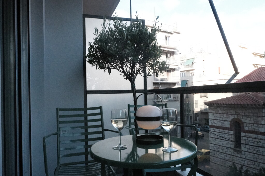 Balcony with round table, wine glasses and an olive tree overlooking Athens